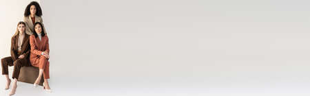 young multicultural women in stylish suits looking at camera on white, bannerの写真素材