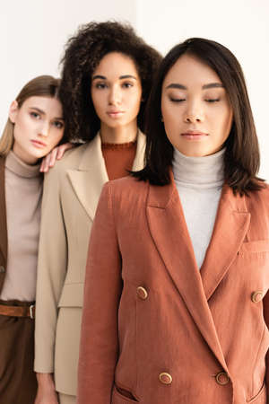 asian woman in suit standing near multicultural friends on white and blurred backgroundの写真素材