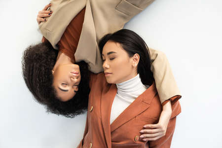 top view of asian and african american women in stylish suits lying on white