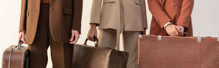partial view of young women in trendy suits holding suitcases isolated on white, bannerの写真素材