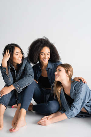 young interracial women in denim outfit smiling while posing on whiteの写真素材
