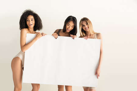 happy interracial women holding blank placard isolated on whiteの写真素材