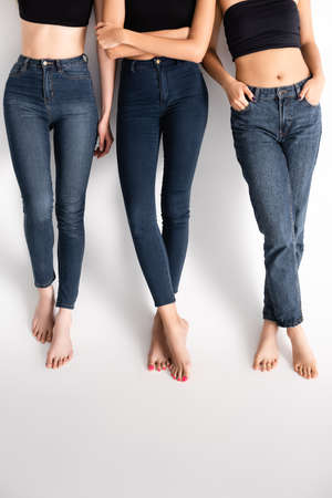 cropped view of young women in denim jeans posing on whiteの写真素材