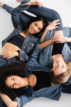 top view of young interracial women in denim outfit posing on whiteの写真素材