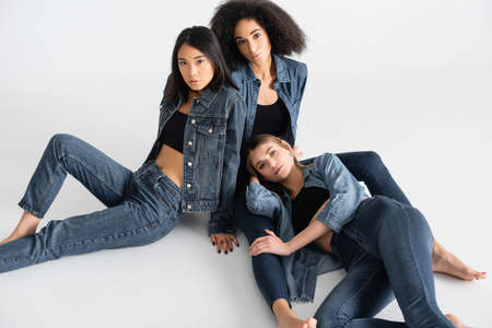high angle view of young interracial women in denim outfit posing on whiteの写真素材
