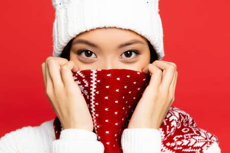 young asian woman in white hat covering face with red scarf with ornament isolated on redの写真素材