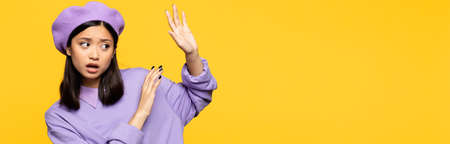 asian woman in beret showing no gesture with hands isolated on yellow, banner
