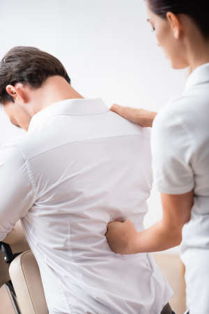 Masseuse massaging back of businessman sitting on massage chair on blurred backgroundの写真素材