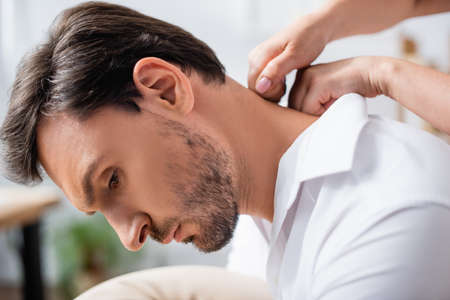Close up view of masseuse massaging neck of bearded businessman on blurred backgroundの写真素材