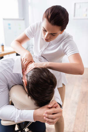 Masseuse doing seated massage of businessman neck in office on blurred backgroundの写真素材