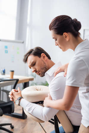 Masseuse doing seated massage of businessman shoulder in office on blurred backgroundの写真素材