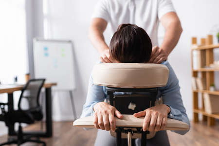 Front view of masseur doing seated massage of shoulders for businesswoman with blurred office on backgroundの写真素材