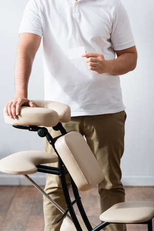 Cropped view of masseur standing near massage chair and holding blank business cardの写真素材