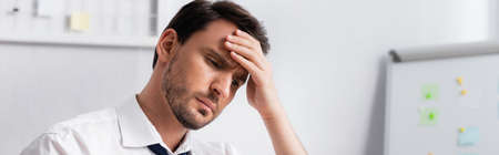 Exhausted businessman with migraine holding hand on forehead, while looking away on blurred...