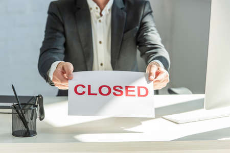 Cropped view of businessman holding sign with closed lettering, sitting at workplaceの写真素材