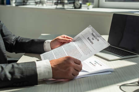 Cropped view of businessman holding petition for bankruptcy, while sitting at workplace on blurred backgroundの写真素材