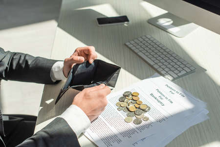 Cropped view of businessman holding empty wallet near coins and petitions for bankruptcy on...
