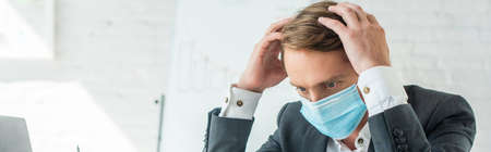 Businessman in medical mask holding hands near head with blurred flipchart on background, banner
