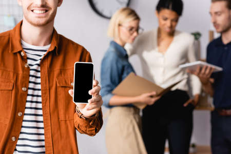 smiling manager showing smartphone with blank screen near multiethnic businesspeople communicating...