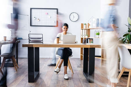 happy african american manager working at laptop in open space office, motion blurの写真素材