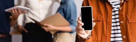 partial view of businessman showing smartphone with blank screen near blurred colleagues on...