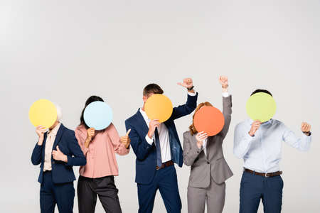 Multicultural businesspeople showing like gesture while covering faces with cards isolated on grayの写真素材