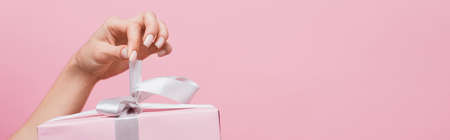 partial view of woman holding ribbon on wrapped present isolated on pink, bannerの写真素材