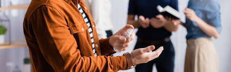 partial view of manager spraying sanitizer on hands near businesspeople on blurred background,...