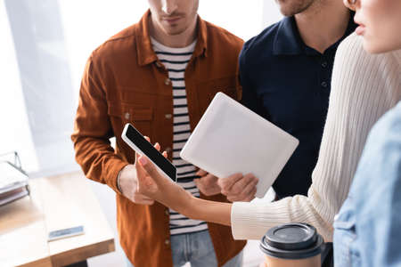 cropped view of african american woman holding smartphone with blank screen near colleagues on blurred foregroundの写真素材