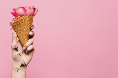 partial view of woman holding waffle cone with petals in hand with flowers covered by plasters...