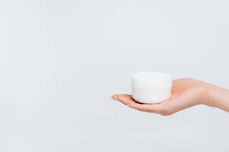 partial view of woman holding jar with moisturizer isolated on whiteの写真素材
