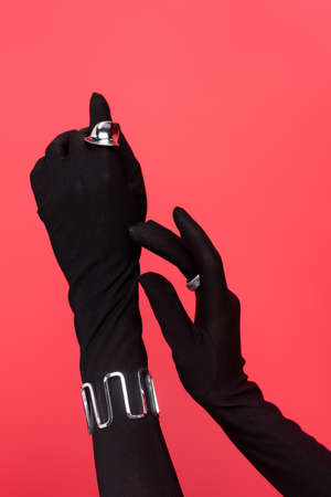 cropped view of female hands in black gloves with rings and bracelet isolated on redの写真素材