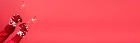 cropped view of woman in mittens holding sparklers isolated on red, bannerの写真素材