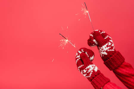 cropped view of woman in mittens holding sparklers isolated on red