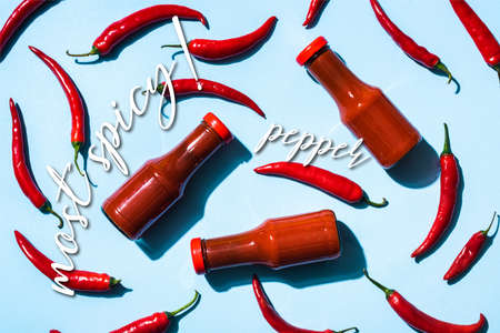 Top view of ripe chili peppers with tomato sauce in bottles near most spicy lettering on blueの写真素材