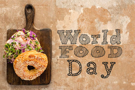 top view of bagel with meat on cutting board with cutlery near world food day lettering on textured surfaceの写真素材