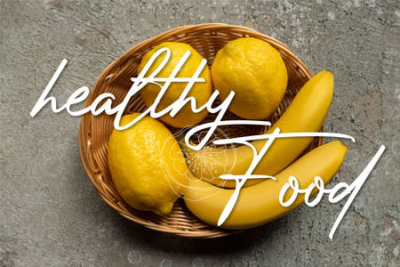 top view of colorful bananas and lemons in wicker basket on gray concrete surface, healthy food illustrationの写真素材