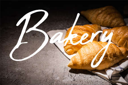 fresh baked croissants on towel near bakery lettering on concrete gray surfaceの写真素材