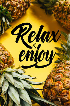 selective focus of fresh ripe pineapples with green leaves on yellow background with relax and enjoy illustrationの写真素材