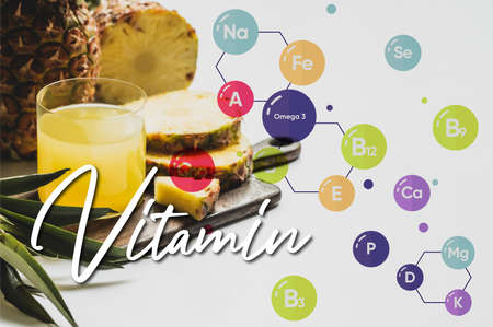 fresh pineapple juice in glass near delicious fruit on wooden cutting board and vitamin lettering on whiteの写真素材