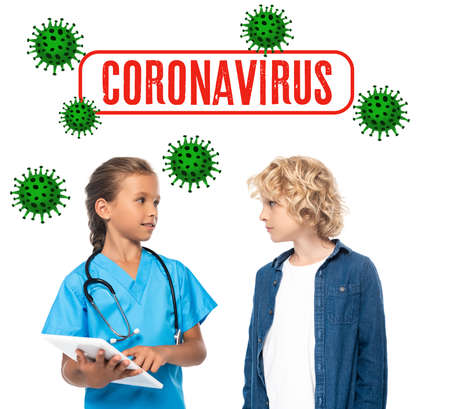 kid in costume of doctor using digital tablet near curly boy and coronavirus lettering on white
