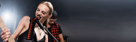 Rock band vocalist with electric guitar singing in microphone with backlit and blurred man on background, bannerの写真素材