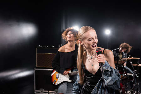 KYIV, UKRAINE - AUGUST 25, 2020: Blonde woman singing with microphone standing near guitarist with...
