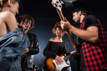 KYIV, UKRAINE - AUGUST 25, 2020: Low angle view of rock band musicians with microphone and electric guitars looking at each other, while talking on blackのeditorial素材