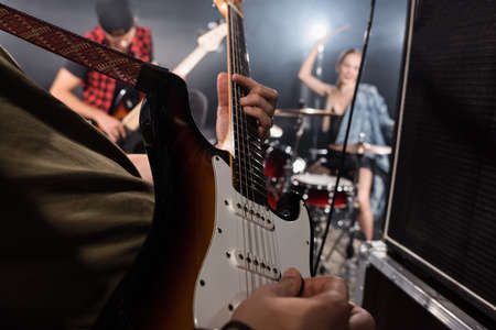 KYIV, UKRAINE - AUGUST 25, 2020: Close up view of man playing electric guitar near combo amplifiers with blurred drummer and guitarist on backgroundのeditorial素材