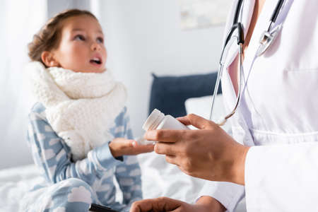 pediatrician giving pills to diseased girl with warm scarf on neck on blurred background