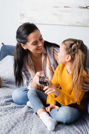 happy woman embracing daughter while holding tv remote controllerの写真素材