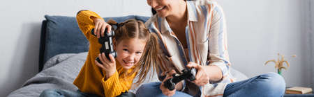 KYIV, UKRAINE - SEPTEMBER 15, 2020: excited woman and child playing video game in bedroom, banner
