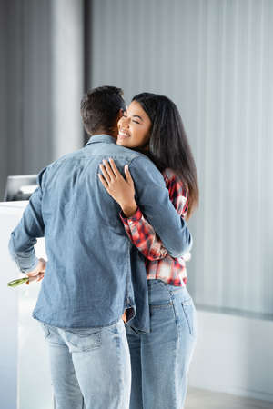 man meeting and hugging happy african american girlfriend in airport