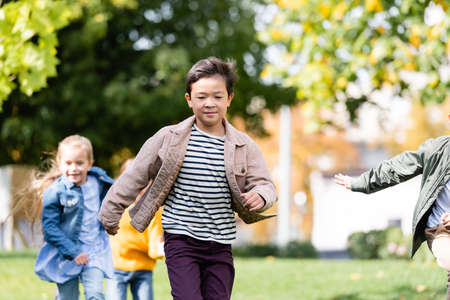 Asian boy running near friends on blurred background in parkの写真素材